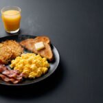 Desayuno americano con huevos, tocino, papas hash, pan tostado, café y jugo.