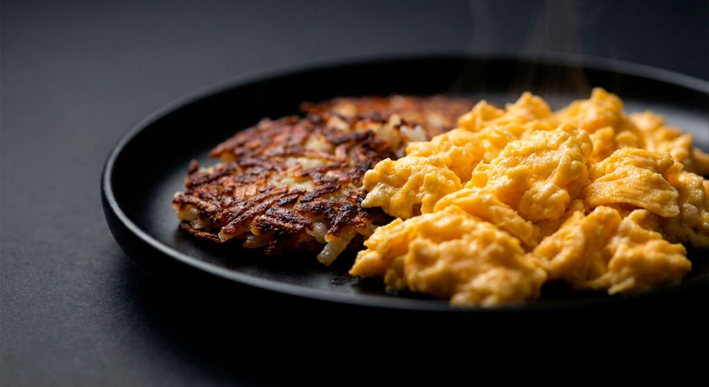 Texturas clásicas del desayuno americano. Detalle de huevos revueltos y papas hash doradas.