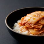 Bowl de arroz con kimchi suave, presentado en cerámica moderna sobre fondo negro con estilo editorial