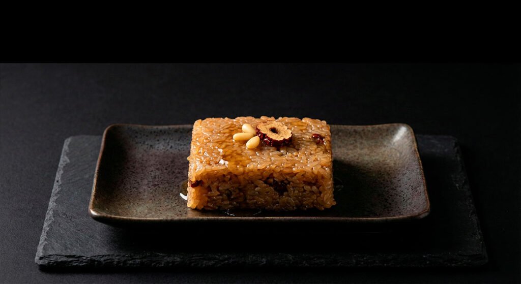 Yakbap (약밥) A square of sweet rice cake garnished with pine nuts and a single dried jujube slice